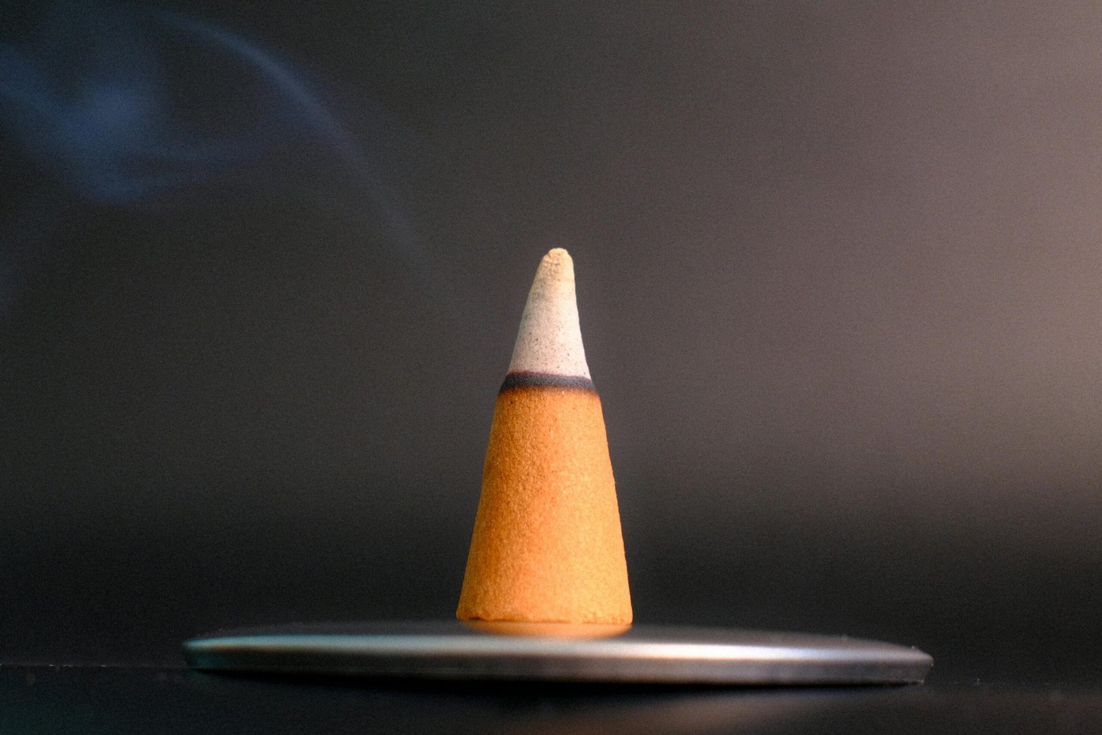 A close-up of a burning incense cone with smoke rising against a dark background, evoking calm and serenity.