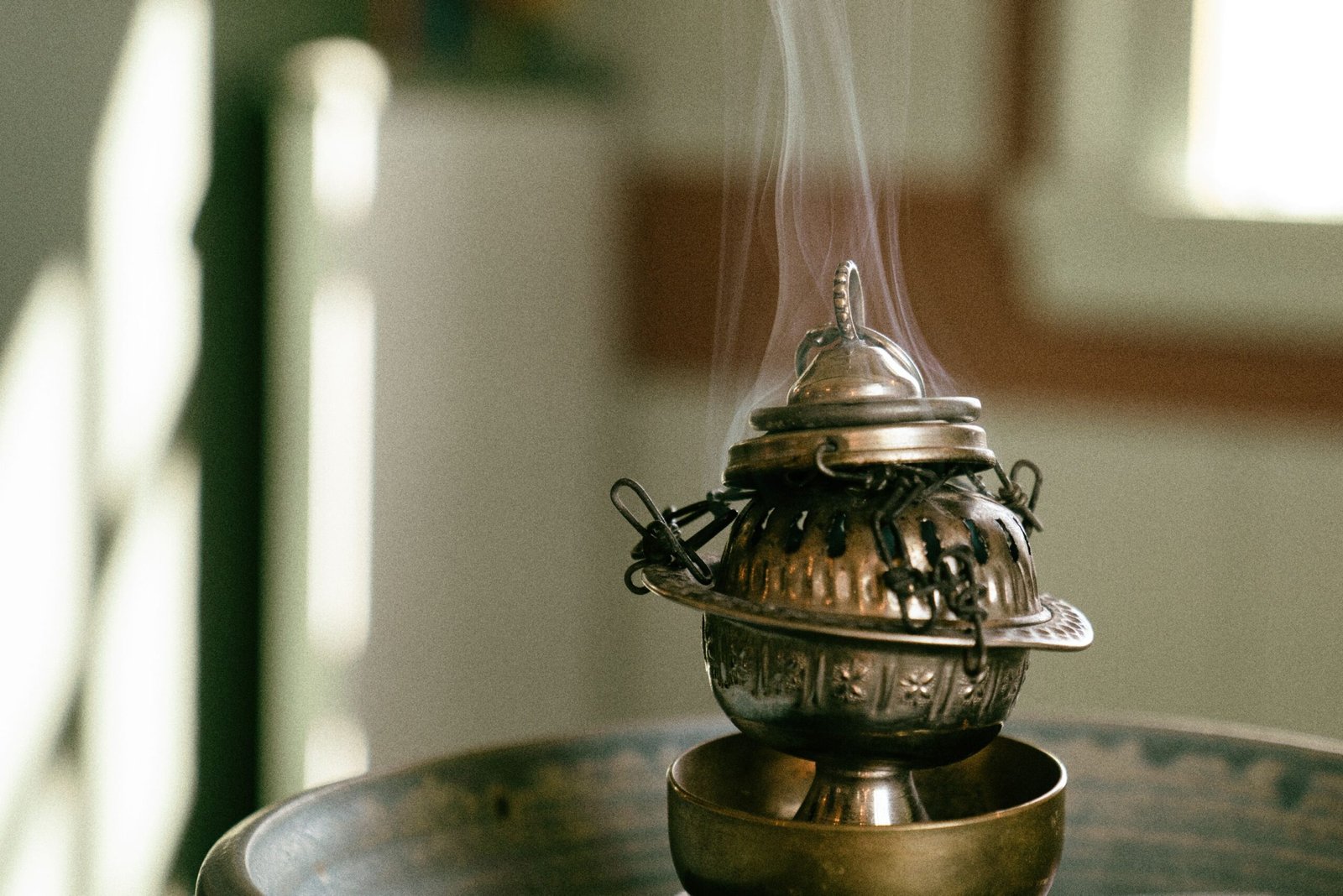 A close-up of a decorative metal censer emitting smoke, creating a tranquil atmosphere indoors.